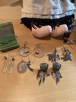 Close-up of various sterling silver Native American earrings and a ring in a green velvet ring box, displayed on a table.