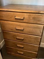 Front view of the tall wooden dresser showing five drawers with wood-fronts and metal handles, visible surface wear on top.