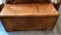 Front view of vintage cedar chest with scratches, stains, and wear visible on exterior wood surface.