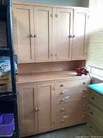 Full view of vintage peach painted hutch showing upper and lower cabinets, drawers, and workshop vise on top.