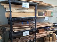 Wide view of the black plastic shelf holding assorted wood pieces labeled 'Lumber' and 'Hardwoods' on signs attached to shelves.