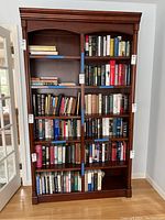 Front view of dark wood bookcase filled with books on multiple shelves showing overall structure and book placement.
