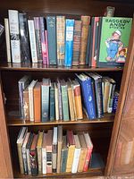 Three shelves filled with books of various genres, mostly older hardcover editions with some wear evident on covers and dust jackets.