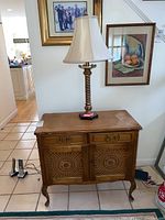 Front side view of wooden cabinet with two drawers and cane inset doors, lamp placed on top.