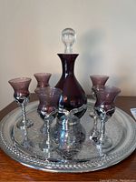 Full set of one decanter and five glasses on a decorative silver tray showing purple colored glass and silver-tone vine motif metalwork