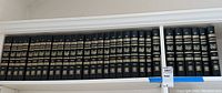 Photo showing entire set of 30 hardcover volumes of Encyclopedia Americana 1995 edition on shelving, spines facing out showing volume numbers and gold embossed titles.