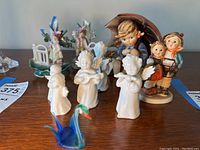 Group of Hummel and angel porcelain figurines with blue glass swan on wooden surface
