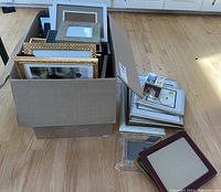 Box containing a variety of picture frames in different materials and finishes, illustrating the overall quantity and diversity in the lot.