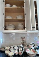 Three wooden shelf cabinet with white plates and bowls and counter with pink wild rose floral patterned dinnerware items including cups, bowls, creamer, sugar bowl and serving bowls.