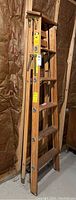Photo showing several wooden ladders stacked in a basement against an insulated wall, showcasing their overall construction and condition.
