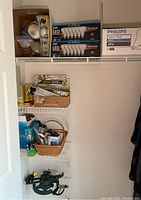 Shelving showing boxes of Enhance LED light bulbs, various miscellaneous boxes including a carbon monoxide detector, lawn sprinkler parts, hose attachments, and a flashlight near the bottom shelf.