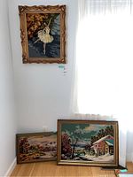 Three framed needlepoints displayed against a wall, showing their relative size and appearance.