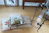 Photo showing two embroidered floral pillows, one inspiration pillow, and metal plate stand on hardwood floor.