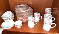 Overview of stacked plates and saucers, bowls on left and mugs on right on wooden shelf