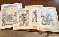 Four black and white signed prints showing village and rural scenes on a tabletop