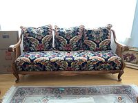 Front view of sofa showing floral upholstery, carved wooden frame, and three pillows