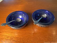Two sterling silver salt servers each with cobalt blue glass inserts and matching spoons on a wooden surface.