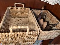 Two rectangular woven baskets, one empty and the other holding several aged wooden shoe molds and shoe stretchers.