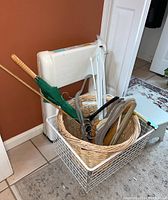 Photo shows woven basket with clothes hangers, green umbrella, and white folding step ladder with white wire basket underneath and small blue step stool nearby