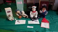 Four dolls displayed with certificates and original boxes, featuring different characters with realistic porcelain faces and fabric clothing.