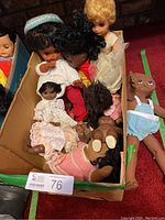 Box filled with assorted vintage plastic dolls in various outfits and sizes, including dolls with bonnets, dresses, and casual clothes.