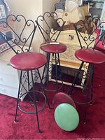Three black metal bar stools with decorative scrollwork and red vinyl seats, plus two additional replacement seats (red and green) on the floor.