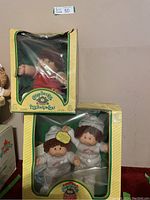 Single Cabbage Patch Kids doll in red overalls in original packaging with box damage visible.