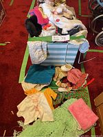Full box of assorted doll clothes and some accessories visible on red carpet.