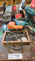 Overview of the lot showing Makita cordless drill, Black & Decker drill, charger, battery and drill bits scattered and in containers on a workbench.