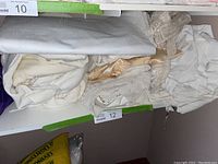 Assorted folded white, cream and gold-tone fabrics stacked on a shelf including lace and crochet details.