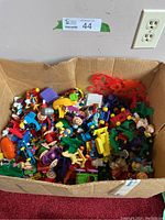 Box filled with assorted colorful McDonald's Happy Meal toys and figures, showing a variety of characters and small parts.