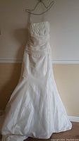 Front view of white wedding gown with ruched midsection and pleated strapless bodice on hanger
