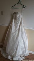 Full view of the dress hanging, showing front silhouette and strapless bodice with embroidered hem detail.