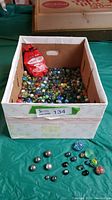 Photo showing a box filled with numerous marbles of various sizes and colors with a red Montrose bag labeled 101 pieces inside.
