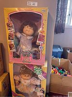 Shows two boxed Cabbage Patch Kids dolls stacked: the Growing Hair doll on top and Happy Birthday doll below