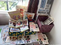 Overview of a collection of vintage sewing patterns, knitting patterns, some rub-on sheets, paper craft materials, and a decorative storage box, all arranged on a table.