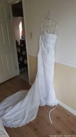 Full-length view of the white wedding dress hanging on a hanger showing the long train and fitted silhouette