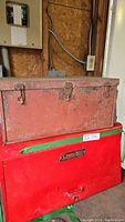 Vintage red steel toolbox stacked on top of red Snap-on 6 drawer fold-top tool box in a workshop setting.