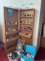 Full view of wooden thread case opened, showing all shelves with spools and accessories, including blue box on floor with more threads.