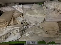 Shelf with rolls and folded white and cream fabrics, some embroidered and lace edged