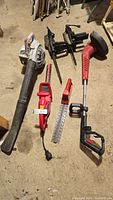 Photo showing a handheld Echo gas blower, Homelight corded hedge trimmer, and other yard tools on floor.
