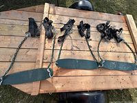 Three green plastic seat swings laid out on a wooden surface showing chains and black straps with hooks.