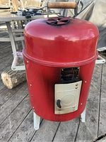Front view of red cylindrical smoker with dent on lid and wooden handle.