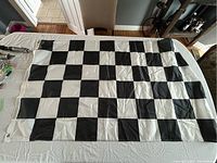 Full view of black and white checkered flag spread out on table, showing all checkered squares and grommets on the left side.