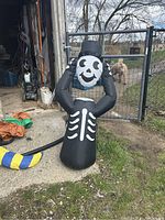 Photo of black inflatable Halloween decoration in the shape of a headless monster with a white skull face and skeleton ribs, standing outdoors near a chain link fence.