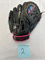 Black Mizuno baseball glove positioned with back side up, showing woven basket pattern and pink and blue diamond accents on back of glove with wrist strap and Mizuno logo.