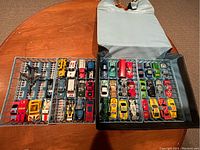 Overview of two trays filled with various small die-cast cars inside a grey plastic carrying case