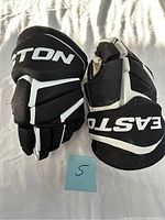 Pair of black and white Easton hockey gloves, size 5 visible on blue note, front padded view