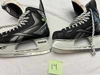 Side view of both black and silver Reebok skates showing the laces, blades marked Reebok, and overall condition.
