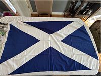 Large Scotland flag with white saltire on blue, laid flat on table showing some wrinkles and signs of needing cleaning